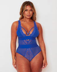 Model wearing the Alicia Fuller Bust Curvy Girl Bodysuit in Bluebird Blue, featuring a plunging neckline with decorative strappy detailing, lace-trimmed cups, sheer mesh panelling, and a sculpting high-waisted silhouette designed for fuller bust support.