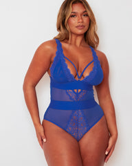 Model posing in the Alicia Fuller Bust Curvy Girl Bodysuit in Bluebird Blue, featuring a deep plunge neckline, lace accents, sheer mesh inserts, and supportive fuller bust construction.