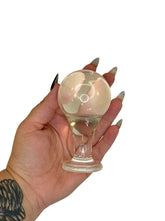 Hand holding a clear glass butt plug against a white background