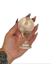 Hand holding a clear glass butt plug against a white background