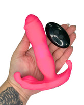 Pink silicone toy held in a hand with a remote control on a white background