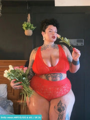 Customer wearing the Hallie Bralette and Brief Set in Chilli Pepper Red from Tutti Rouge, posing indoors while holding flowers. The set features floral lace detailing and a supportive fuller-bust fit.
