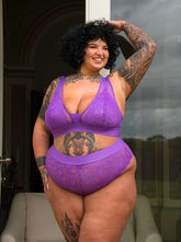 Curvy tattooed model wearing the Hallie Passion Purple lingerie set by Tutti Rouge, posing confidently outside in a sheer lace bralette and matching briefs.