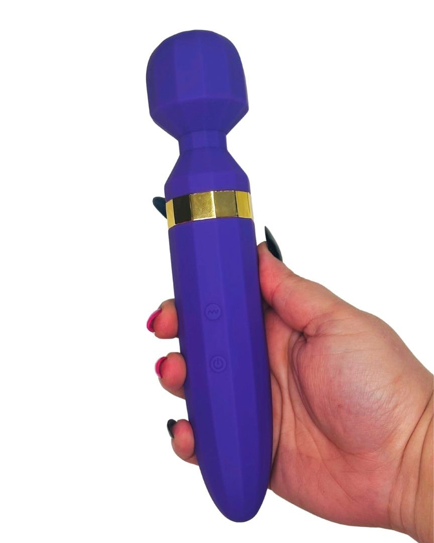 Purple handheld massager with gold accents held in a hand on a white background