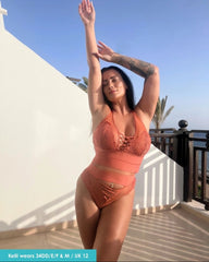 Woman in an orange bikini standing on a balcony with a clear blue sky.