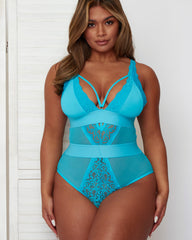 Model posing in the Alicia Fuller Bust Curvy Girl Bodysuit in Bluebird Blue, highlighting the deep plunge neckline, lace accents, sheer mesh inserts, supportive underbust band, and smoothing high-waisted design.