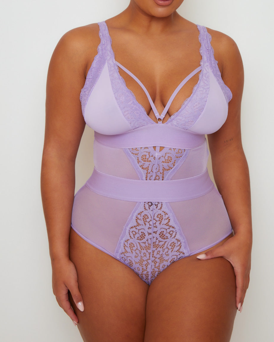 Close-up front view of the Alicia Fuller Bust Curvy Girl Bodysuit in Soft Lavender, showcasing delicate floral lace accents, sheer mesh panelling, wide supportive waistband, and strappy plunge neckline detailing.