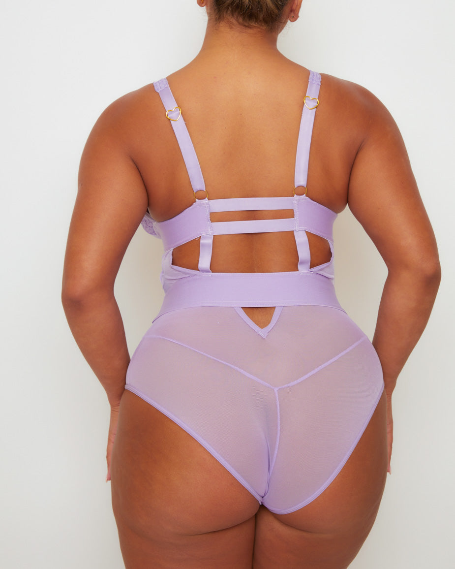 Close-up back view of the Alicia Fuller Bust Curvy Girl Bodysuit in Soft Lavender, showcasing the strappy open-back design, wide waistband, adjustable straps, and semi-sheer mesh finish.