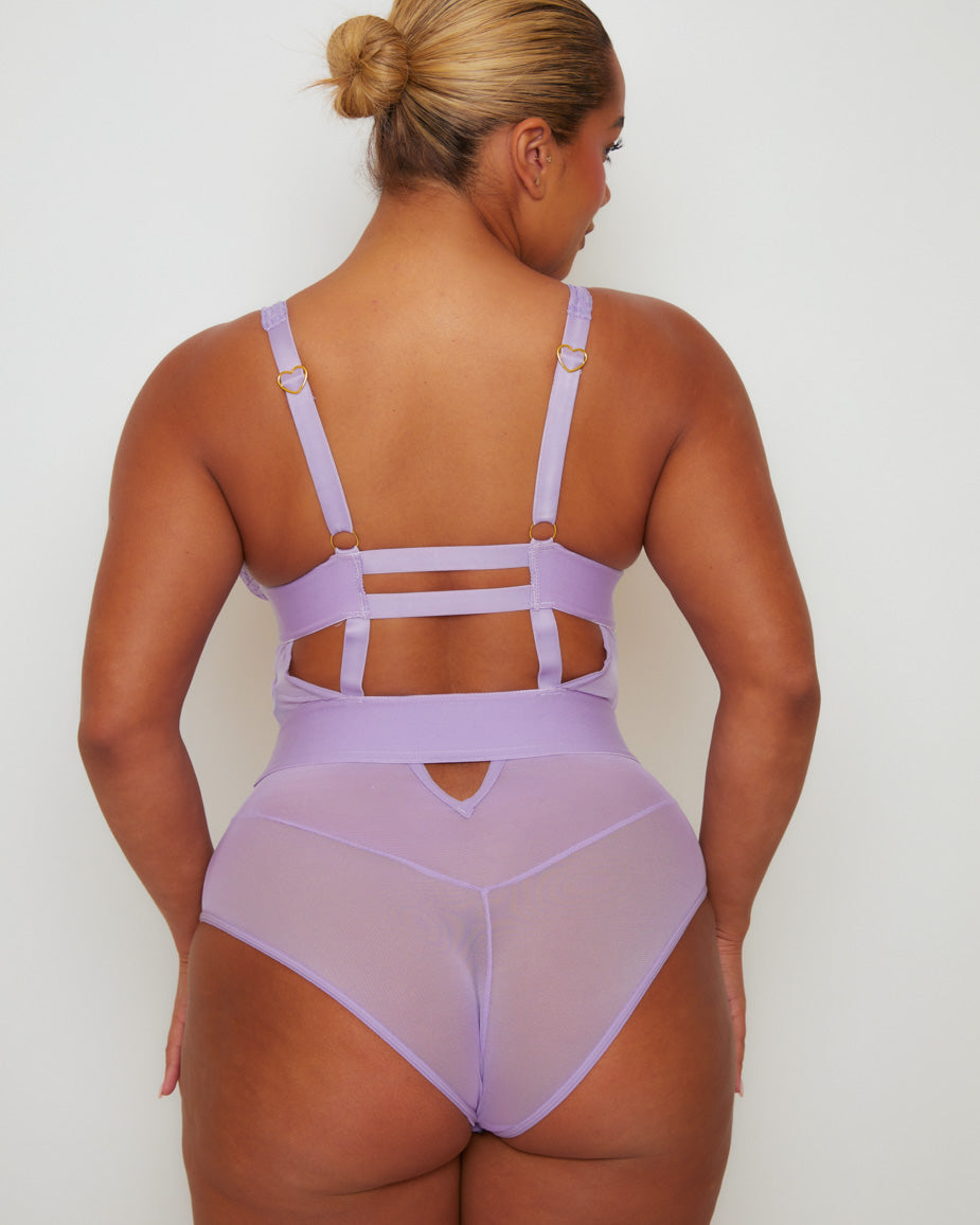 Back view of the Alicia Fuller Bust Curvy Girl Bodysuit in Soft Lavender, featuring adjustable shoulder straps with gold-tone heart hardware, cut-out back detailing, and sheer mesh brief styling.