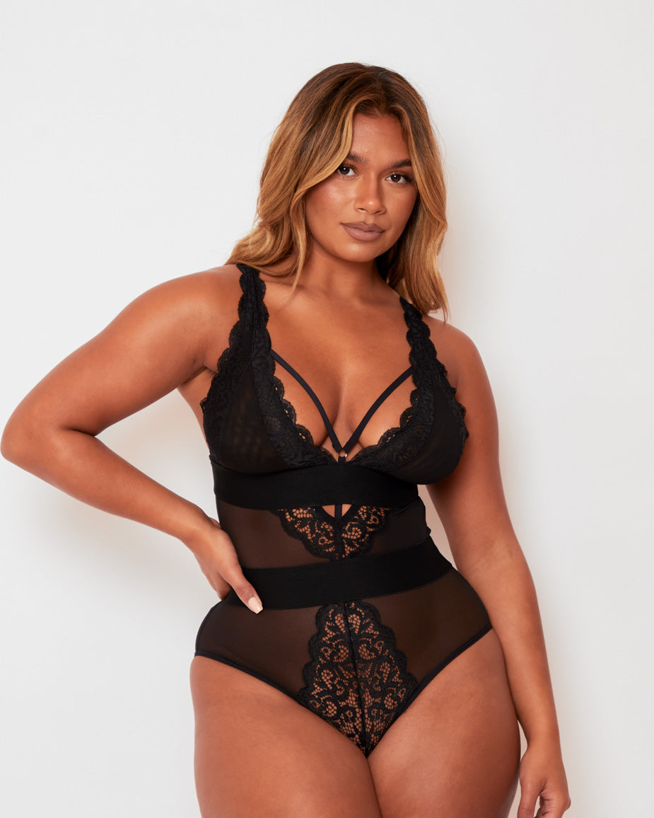 Model posing in the Alicia Bodysuit in Black by Tutti Rouge, displaying sheer mesh panels, intricate lace detailing, and a supportive, figure-enhancing fit.