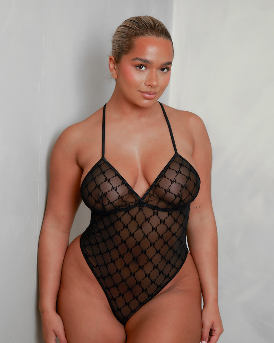 Front view of the Tutti Boudoir Kaylee Bodysuit in Onyx Black, featuring sheer monogram mesh, a plunging triangle neckline, high-cut legs and a sleek, sculpting silhouette designed to flatter every curve.