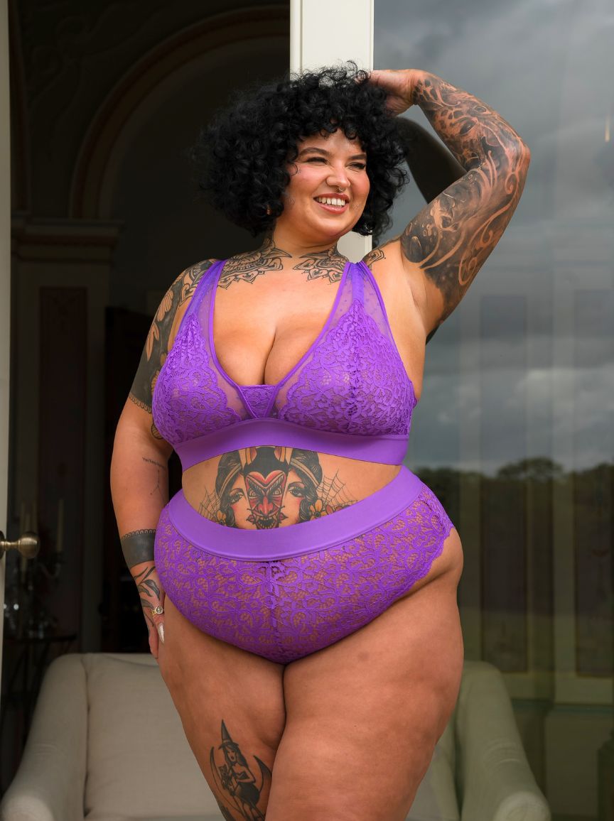 Curvy tattooed model wearing the Hallie Passion Purple lingerie set by Tutti Rouge, posing confidently outside in a sheer lace bralette and matching briefs.